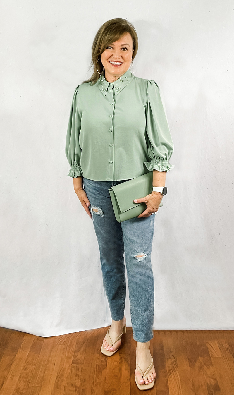 Woman in green embellished top with straight leg jeans and matching bag.